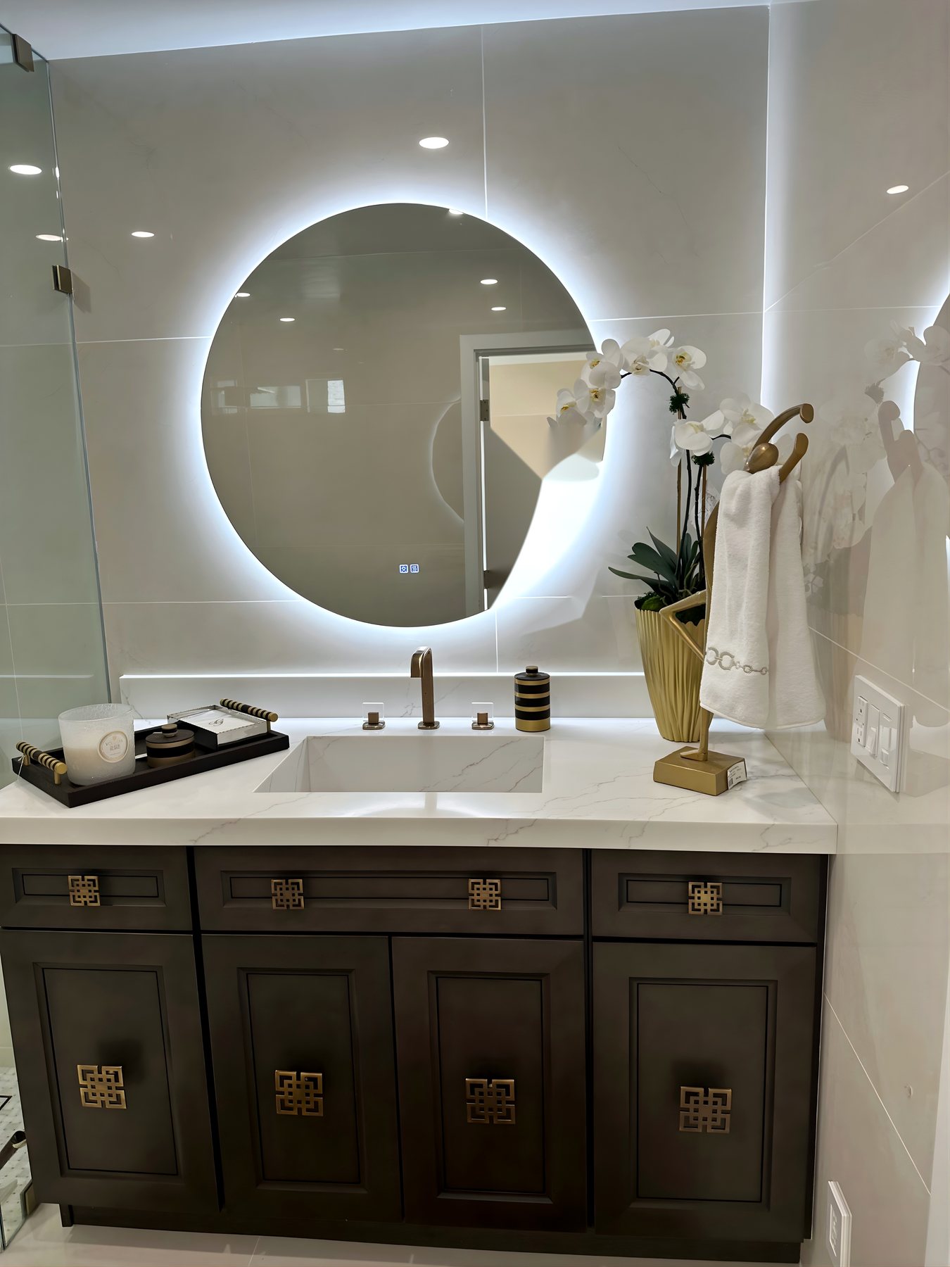Powder bath with dark cabinetry, brass faucet and backlit round mirror